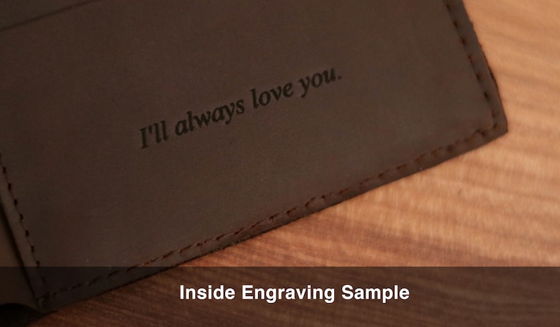 Puede incluir: Primer plano de una cartera de cuero marr&oacute;n con la inscripci&oacute;n "I'll always love you." en el interior. La cartera est&aacute; sobre una superficie de madera. Muestra de grabado interior.
