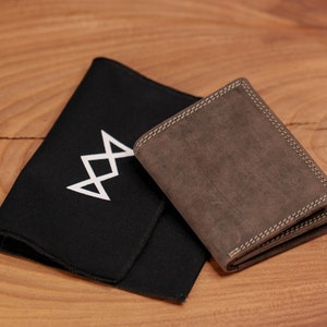 May include: A brown leather wallet with white stitching and a black cloth with a white geometric design. The wallet is rectangular and appears to be made of distressed leather. The cloth is folded and lies next to the wallet.