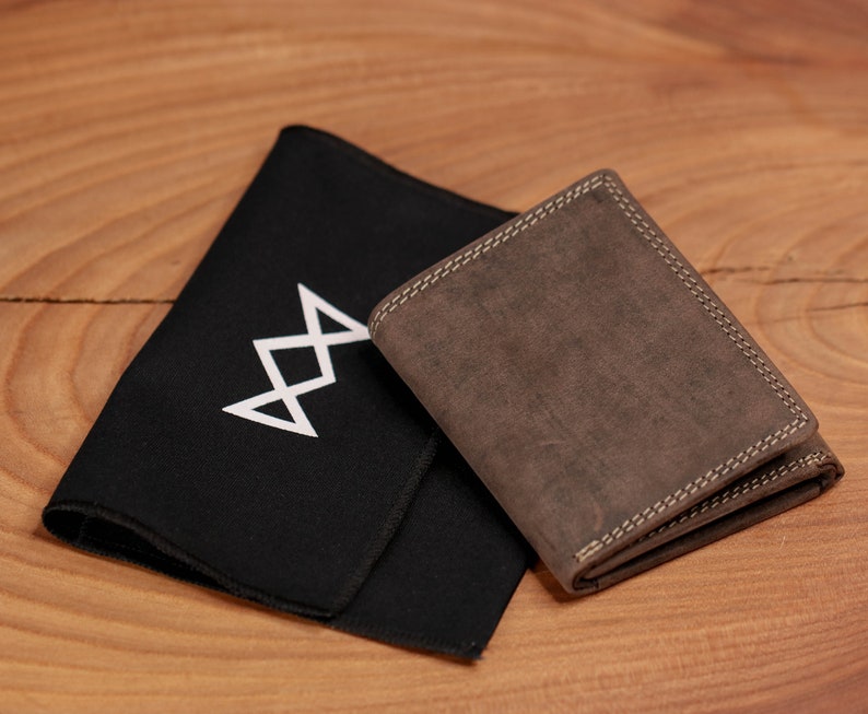 May include: A brown leather wallet with white stitching and a black cloth with a white geometric design. The wallet is rectangular and appears to be made of distressed leather. The cloth is folded and lies next to the wallet.