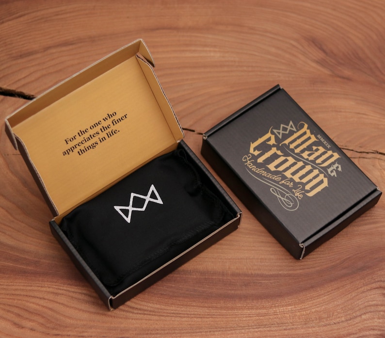 May include: An open cardboard box with the text "For the one who appreciates the finer things in life." A black box with gold text that reads "Mave Crown Handmade for Life" is next to it. Inside the open box is a black pouch with a white geometric design.