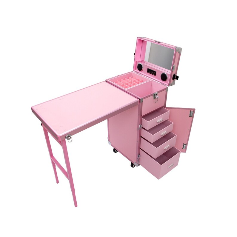 May include: Pink rolling makeup case with a fold-out table, drawers, and a mirror. The case has a top compartment with dividers, speakers, and a handle. The table is supported by pink legs. The case is designed for beauty professionals.