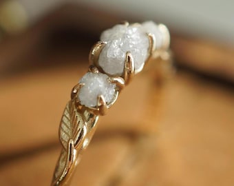 Op de afbeelding: Een gouden ring met drie ruwe diamanten gezet in een bladontwerp.