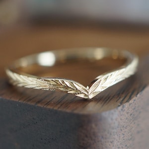 Puede incluir: Un anillo de oro con un diseño en forma de V y un patrón de hojas.
