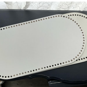 May include: Two off-white, oval-shaped bases with rounded edges, featuring a series of evenly spaced circular holes punched along the entire perimeter. These flat, smooth panels are designed for crafting projects and are stacked slightly offset.