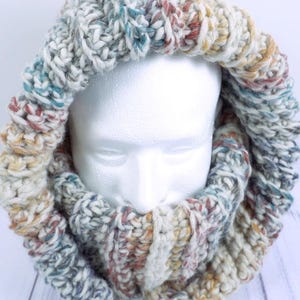 May include: A chunky knit cowl in a variety of colors, including blue, yellow, and red. The cowl is made of thick yarn and is designed to be worn around the neck. The knitted cowl is displayed on a white mannequin head.