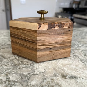 May include: A hexagonal wooden box with a light wood top and a dark wood bottom. The box has a brass knob on the top.