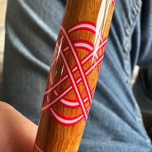 May include: A wooden pen with a red and white geometric design. The pen is made of wood with a natural grain and has a glossy finish.
