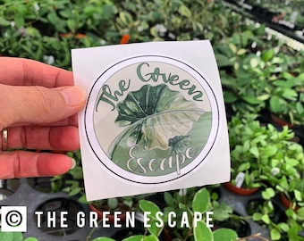 May include: A white sticker with a green circle and the text "The Green Escape" in a white circle. The circle features a green leaf with white veins.