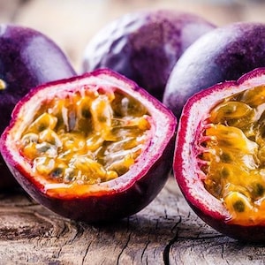 May include: Close-up of several passion fruits, some whole and others halved, revealing the vibrant yellow pulp and seeds. The fruits have a deep purple skin and are arranged on a rustic wooden surface.