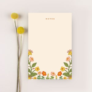 Puede incluir: Un bloc de notas con un borde floral en tonos naranja, amarillo y rosa. El bloc de notas tiene la palabra "NOTES" impresa en marr&oacute;n en la parte superior.