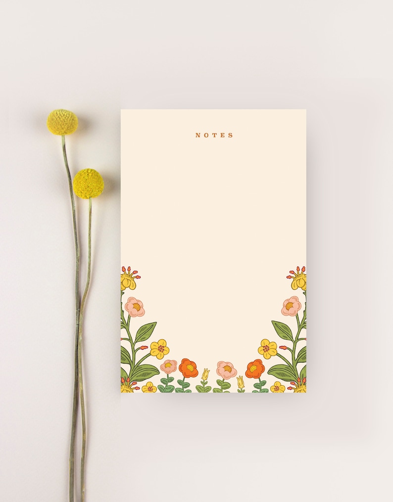 Puede incluir: Un bloc de notas con un borde floral en tonos naranja, amarillo y rosa. El bloc de notas tiene la palabra "NOTES" impresa en marr&oacute;n en la parte superior.
