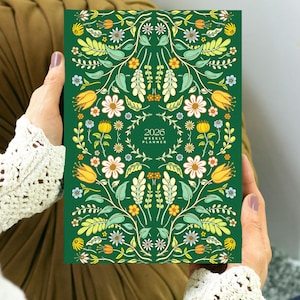 Cute 2026 weekly planner featuring folk cover floral illustration. The planner is bound like a book and it's compact and light.