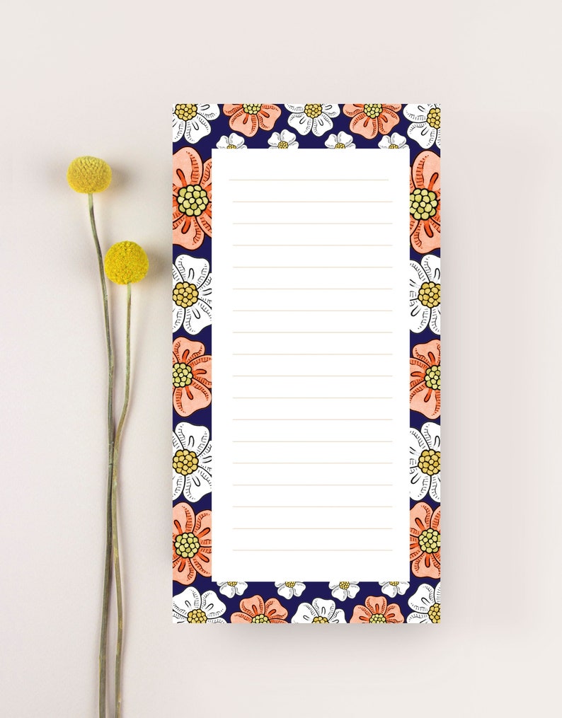 May include: A white notepad with a blue border and a floral pattern. The flowers are pink, white, and yellow. The notepad has lined paper for writing.