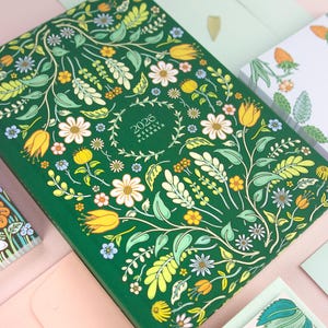 Hardcover yearly planner with bright and colorful cover design featuring folk, cottagecore style artwork.