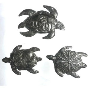 May include: Three silver metal turtle ornaments with a floral design. The turtles are all facing the same direction and have a raised design on their shells.