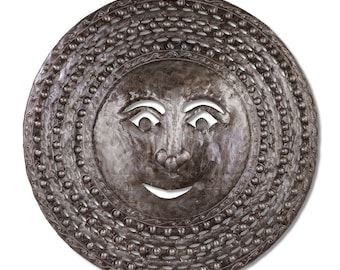 May include: A circular metal sun face wall decoration. The sun features a smiling face with cut-out eyes and mouth. The face is encircled by decorative metalwork, including a beaded border. The metal has a textured finish.