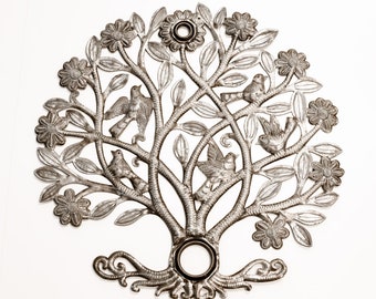 May include: A silver metal wall art piece depicting a stylized tree with birds and flowers. The tree has a circular opening at the top and bottom.