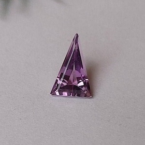 May include: A triangular shaped amethyst gemstone with a purple hue.