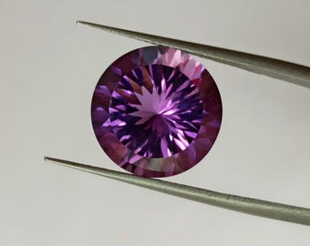 Könnte beinhalten: Ein runder, facettierter Edelstein in leuchtendem Violett mit einem sternförmigen Muster, das von der Mitte ausstrahlt. Der Stein weist präzise geometrische Schliffe auf, die Lichtreflexionen auf der Oberfläche erzeugen, gehalten von einer Pinzette.