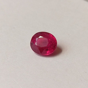 May include: A deep red gemstone with a faceted cut. The gemstone is round and has a high polish.