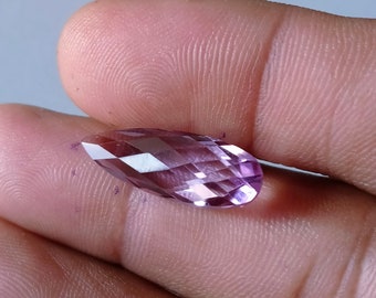 May include: A marquise-cut gemstone with a translucent light purple hue and a faceted surface. The stone features a pointed, elongated shape with multiple geometric facets that reflect light, creating a sparkling appearance across its surface.