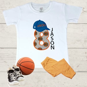 May include: White t-shirt with a blue and orange number 8, a blue baseball cap with the word "KNICKS" on it, and the name "JASON" on the shirt. A basketball, a pair of black sneakers, and a pair of orange pants are also pictured.