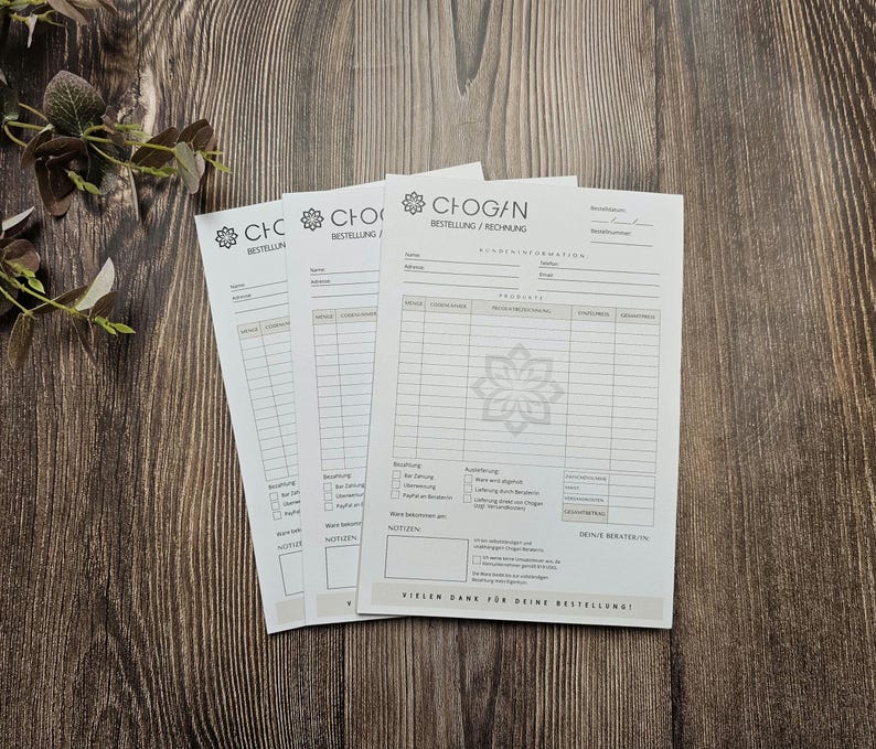 May include: Three white order forms with the text "CHOGAN BESTELLUNG/RECHNUNG" at the top. The forms have a black floral design and are on a wooden surface.