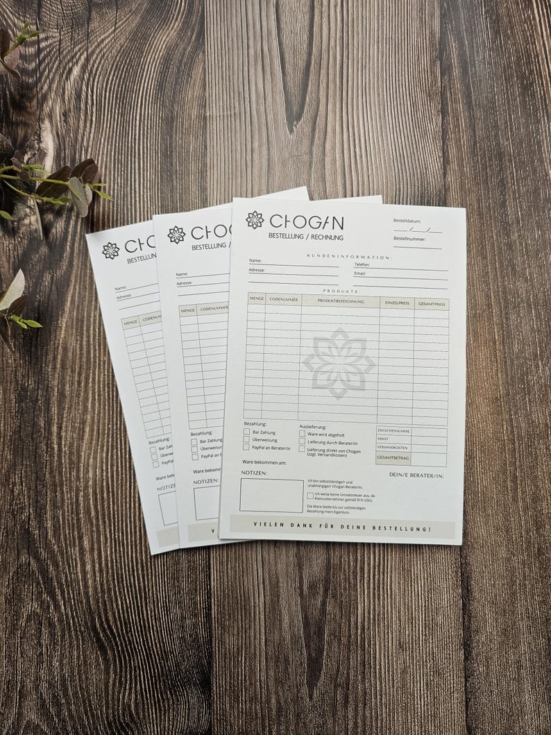 May include: Three white order forms with the text "CHOGAN BESTELLUNG/RECHNUNG" at the top. The forms have sections for customer information, products, prices, and payment details. The forms also include a section for notes and a space for the customer's advisor's name. The forms are on a wooden surface.