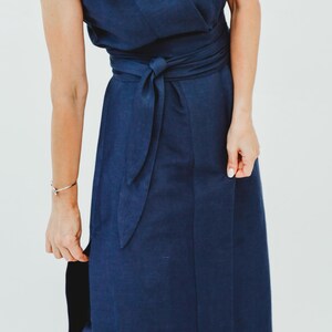 May include: A sleeveless navy blue wrap dress with a matching waist tie. The dress has a flowing skirt and a wrap-style bodice. The fabric appears to be linen or a similar lightweight material. The dress is a solid color and suitable for various occasions.
