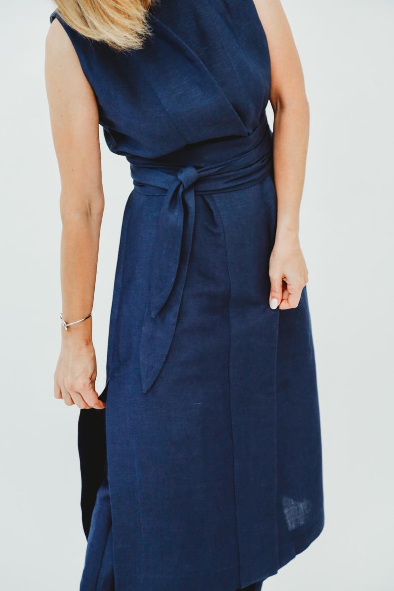 May include: A sleeveless navy blue wrap dress with a matching waist tie. The dress has a flowing skirt and a wrap-style bodice. The fabric appears to be linen or a similar lightweight material. The dress is a solid color and suitable for various occasions.