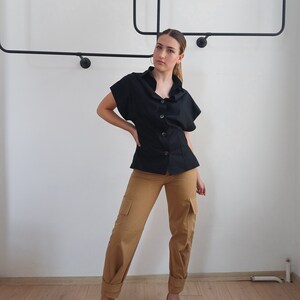 May include: A black button-down top with short sleeves and tan cargo pants. The pants have pockets on the sides and are cuffed at the ankles. The person is wearing green heels.