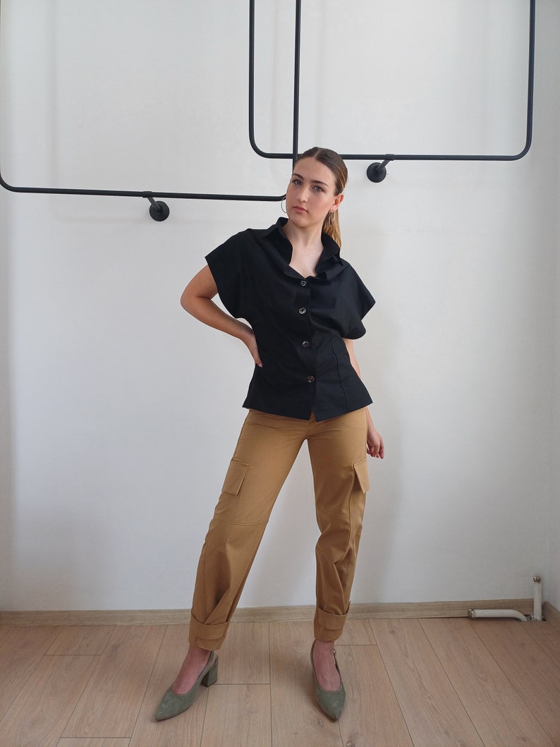 May include: A black button-down top with short sleeves and tan cargo pants. The pants have pockets on the sides and are cuffed at the ankles. The person is wearing green heels.