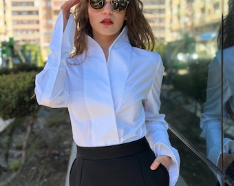May include: A crisp white long-sleeved button-down shirt with a high standing collar and wide cuffs, paired with a high-waisted black skirt. The shirt features a clean, structured front placket and long sleeves, while the skirt has a smooth, solid black finish.