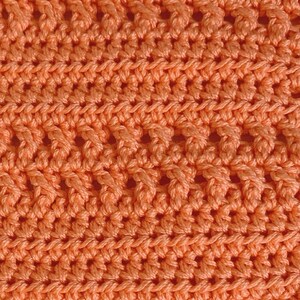 K&ouml;nnte beinhalten: Nahaufnahme eines geh&auml;kelten Stoffes mit einem sich wiederholenden Rautenmuster in einer leuchtenden Korallenfarbe.