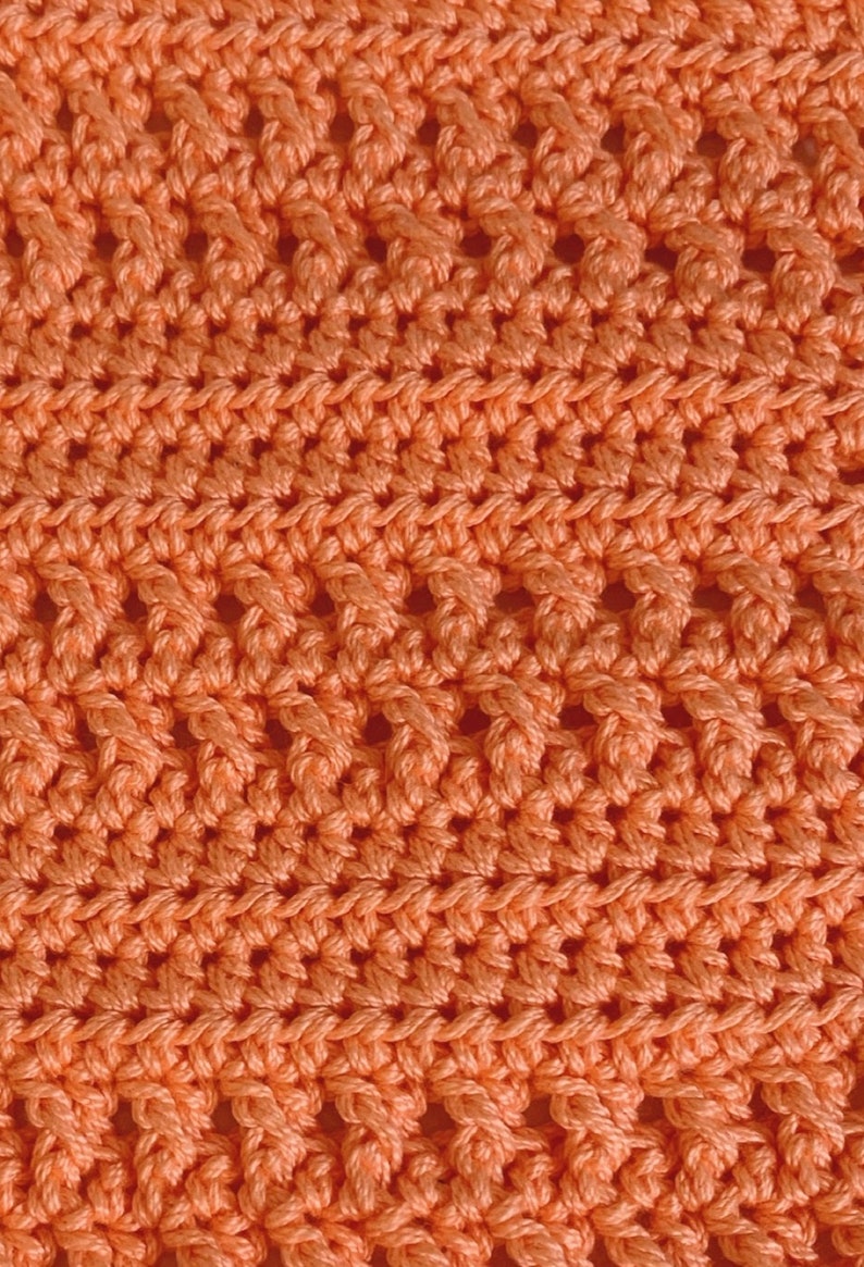 K&ouml;nnte beinhalten: Nahaufnahme eines geh&auml;kelten Stoffes mit einem sich wiederholenden Rautenmuster in einer leuchtenden Korallenfarbe.