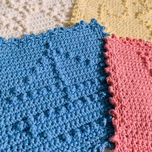 Puede incluir: Cuatro pa&ntilde;os de cocina de ganchillo en diferentes colores: blanco, amarillo, azul y rosa. Los pa&ntilde;os de cocina son todos cuadrados y tienen un borde festoneado.