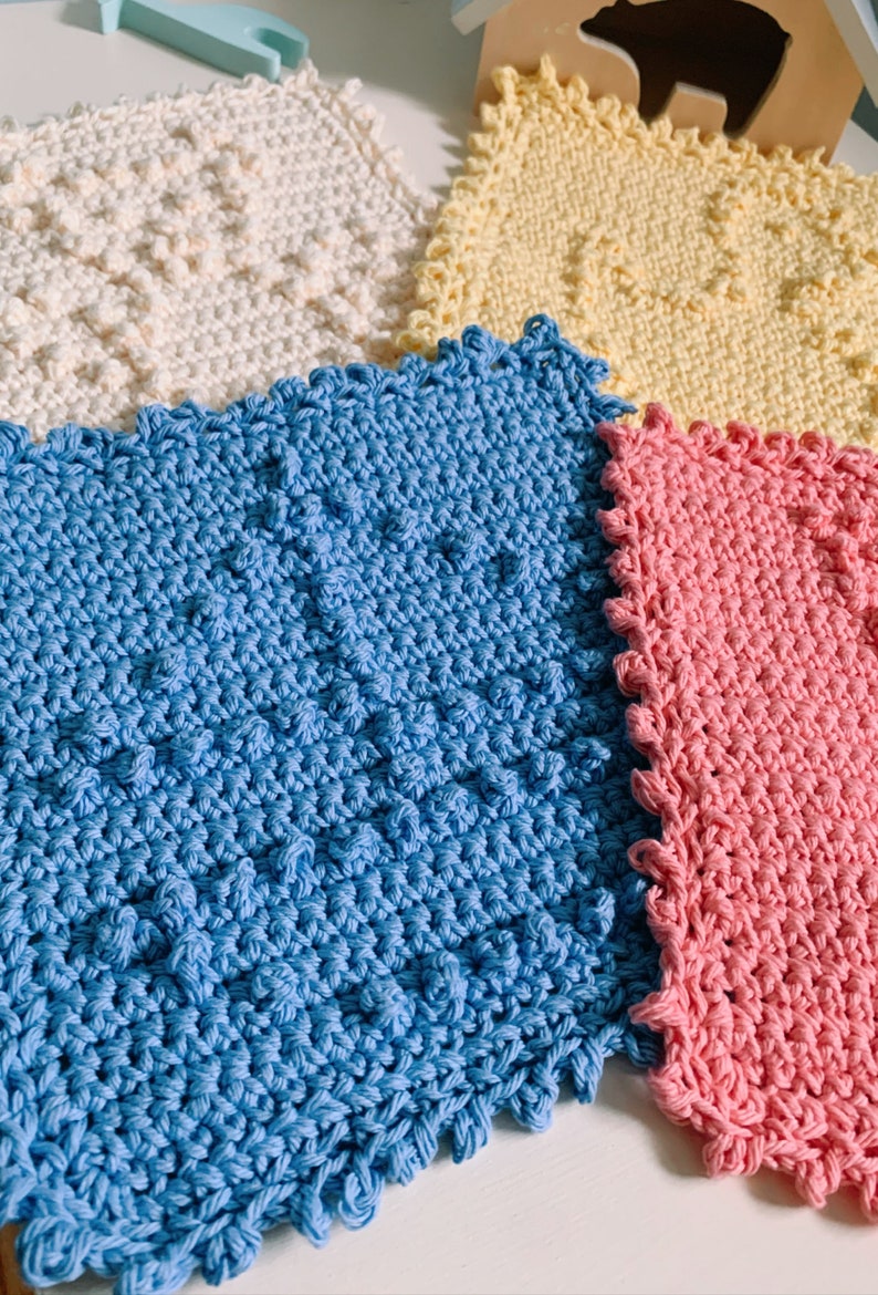 Puede incluir: Cuatro pa&ntilde;os de cocina de ganchillo en diferentes colores: blanco, amarillo, azul y rosa. Los pa&ntilde;os de cocina son todos cuadrados y tienen un borde festoneado.