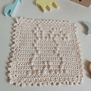 Puede incluir: Un pa&ntilde;o de cocina cuadrado de color crema tejido a crochet con un patr&oacute;n texturizado y un borde festoneado.