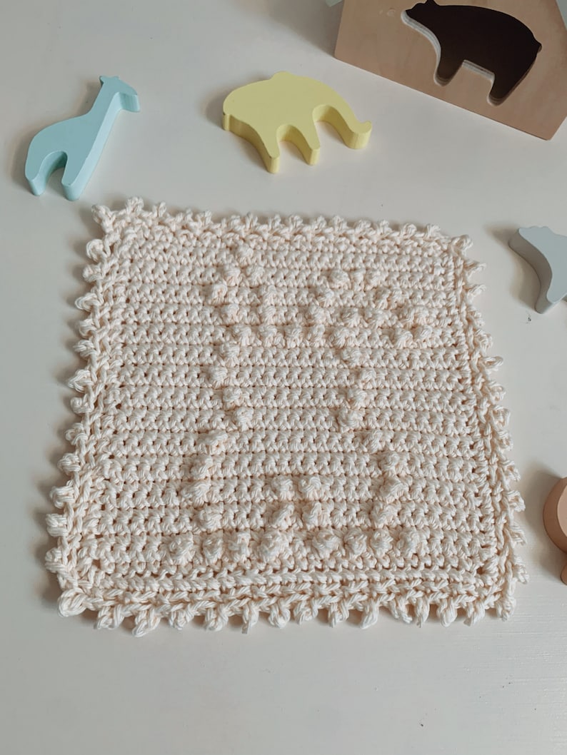 Puede incluir: Un pa&ntilde;o de cocina cuadrado de color crema tejido a crochet con un patr&oacute;n texturizado y un borde festoneado.