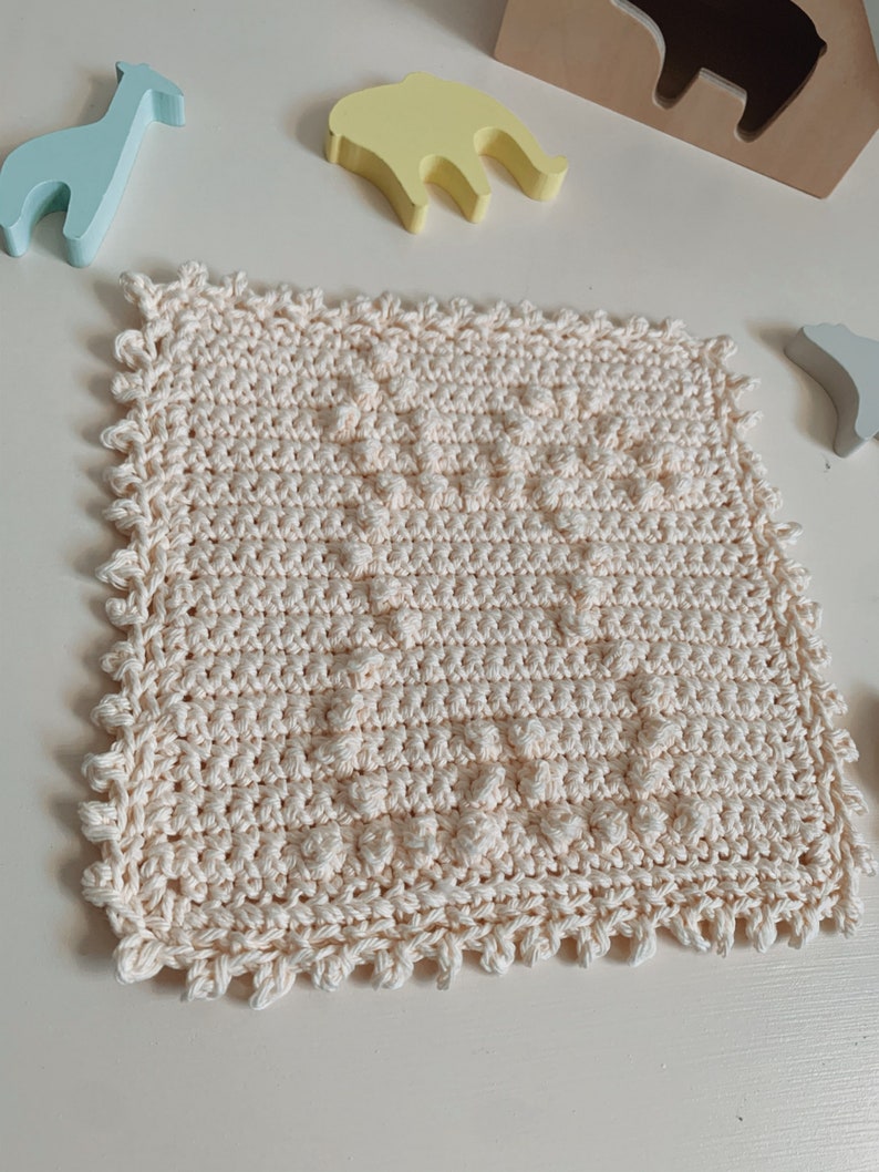 Puede incluir: Un pa&ntilde;o de cocina cuadrado de color crema tejido a crochet con un patr&oacute;n texturizado. El pa&ntilde;o de cocina tiene un borde festoneado.