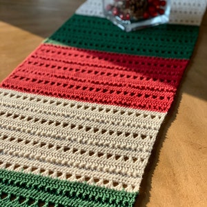 May include: A crocheted table runner with alternating stripes of green, red, and white. The runner has a lacy pattern with small holes throughout.