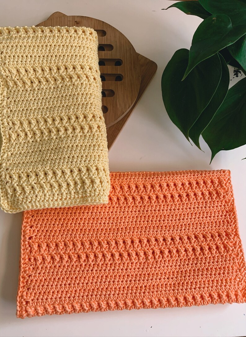 K&ouml;nnte beinhalten: Zwei geh&auml;kelte Geschirrt&uuml;cher, eines gelb und eines orange, mit einem strukturierten Muster. Die Geschirrt&uuml;cher sind mit einem einfachen Stich gearbeitet und perfekt f&uuml;r den t&auml;glichen Gebrauch.