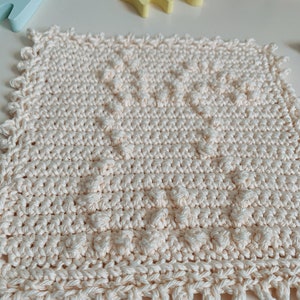 Puede incluir: Un pa&ntilde;o de cocina de crochet de color crema con un patr&oacute;n texturizado. El pa&ntilde;o de cocina tiene un borde festoneado.