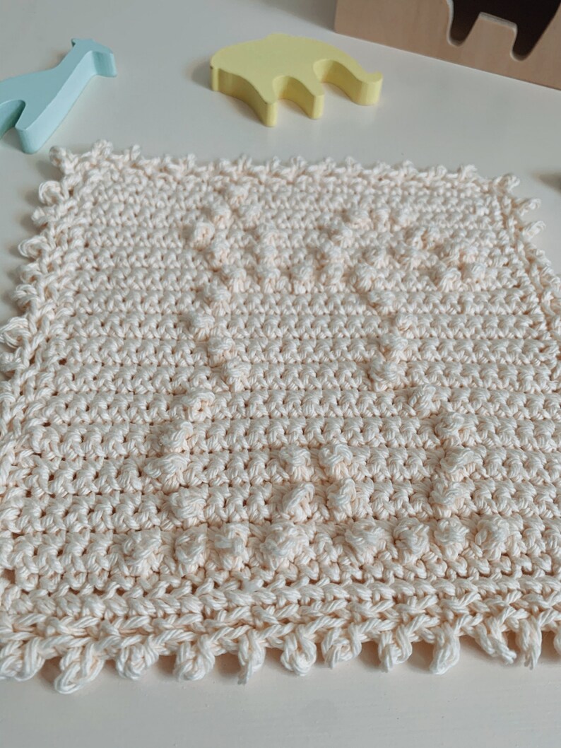 Puede incluir: Un pa&ntilde;o de cocina de crochet de color crema con un patr&oacute;n texturizado. El pa&ntilde;o de cocina tiene un borde festoneado.
