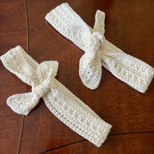 Pode incluir: Duas faixas de cabeça brancas de crochê com laços. As faixas de cabeça são feitas com um padrão de ponto simples e têm um visual delicado e feminino.