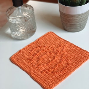 May include: A bright orange crocheted dishcloth or kitchen scrubber. The cloth is made with a simple stitch pattern and has a square shape.