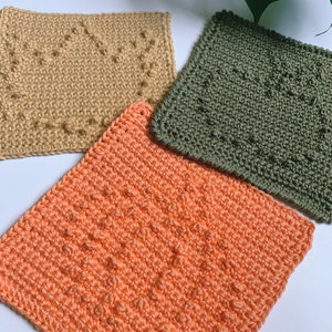 May include: Three crocheted squares in different colours and textures. The squares are beige with a diamond pattern, green with a textured pattern, and orange with a ribbed pattern.