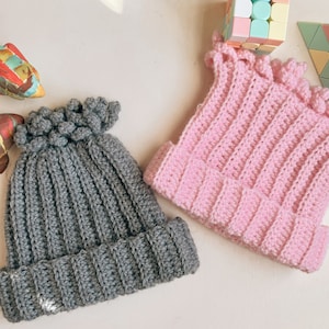 May include: Two crocheted hats, one gray and one pink. Both hats have a ribbed texture and a decorative ruffle around the brim.