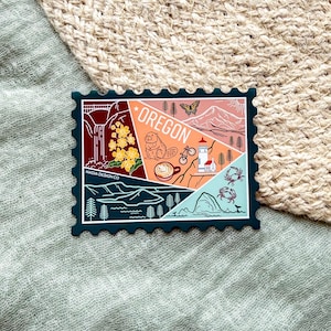 May include: A rectangular sticker with a postage stamp design featuring the word "OREGON" and various illustrations. The sticker has a dark blue border and includes images of a bridge, flowers, a butterfly, and a mountain.