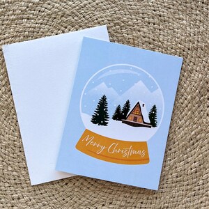 Cartão de globo de neve de Feliz Natal | Cartões dobrados de 4,25” x 5,5” com envelopes | Montanhas, maravilhas do inverno, cabana, bosques, ao ar livre, inverno, natureza